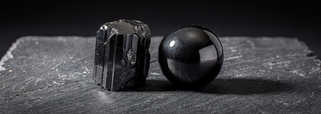 Black tourmaline crystal and shungite sphere on dark slate surface